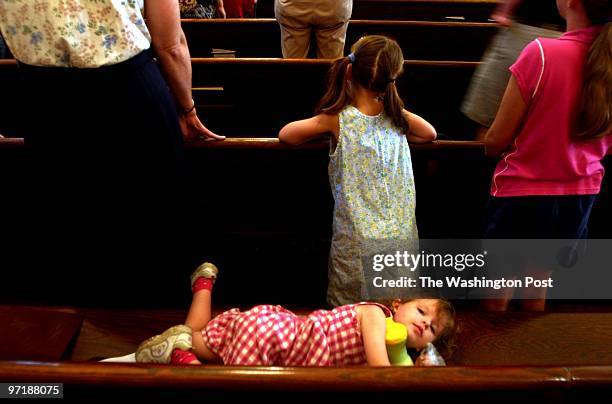 Year old Theresa Gassner fidgets beside her older sisters Katherine and Maggie during 11:00 am Sunday mass at St. Bernadette Catholic Church in...
