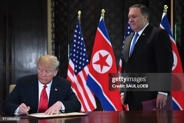 President Donald Trump signs a document while US Secretary of State Mike Pompeo looks on during a signing ceremony with North Korea's leader Kim Jong...