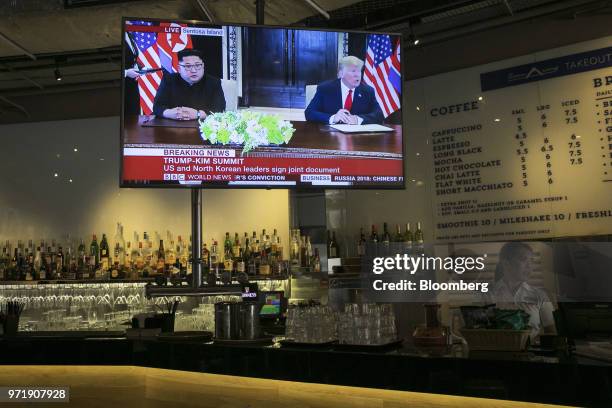 Screen displays a news broadcast of U.S. President Donald Trump and North Korean leader Kim Jong Un attending a document-signing event, at a...