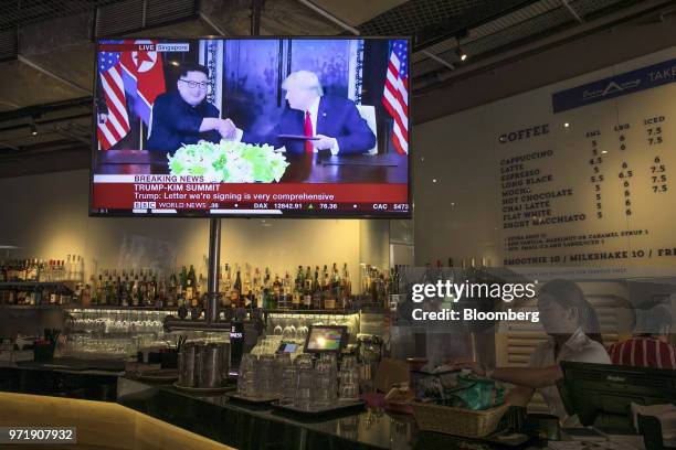 Screen displays a news broadcast of U.S. President Donald Trump and North Korean leader Kim Jong Un shaking hands at a document-signing event, at a...