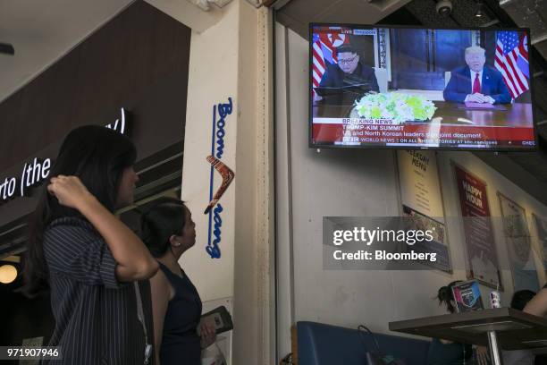 People watch a screen displaying a news broadcast of U.S. President Donald Trump and North Korean leader Kim Jong Un attending a document-signing...