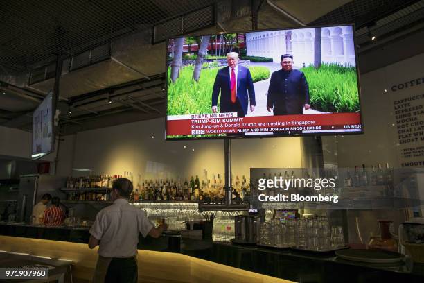 Screen displays a news broadcast of U.S. President Donald Trump and North Korean leader Kim Jong Un attending the DPRK-USA Singapore Summit, at a...