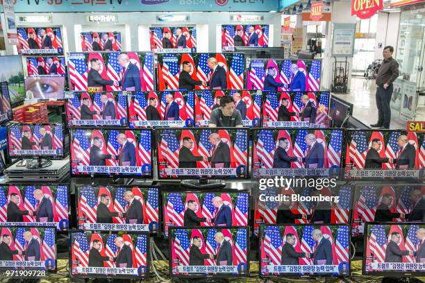 Man stands at a counter as television screens display a news broadcast of U.S. President Donald Trump and North Korean leader Kim Jong Un shaking...