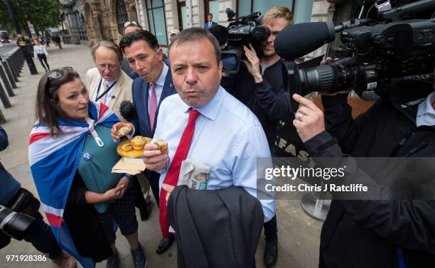 Leave.EU backer Arron Banks eats a pork pie handed to him by an anti-Brexit demonstrator as he arrives to give evidence to the fake news select...