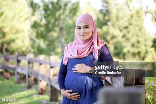 young pregnant women with blue dress holding belly - pregnant muslim stock pictures, royalty-free photos & images