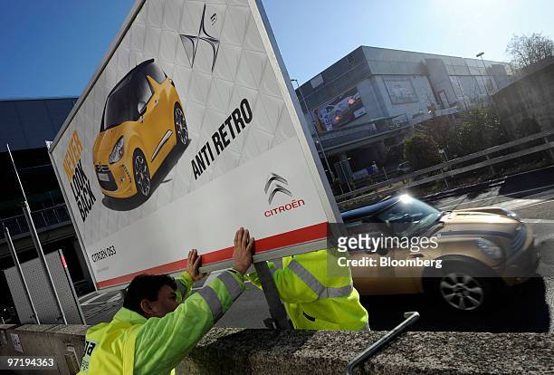 Employees install a sign advertising the Citroen DS3 automobile as a Mini automobile passes prior to the official opening of the Geneva International...