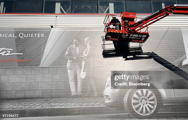 An employee uses a cherry picker to install a Vredestein tires advertisement prior to the official opening of the Geneva International Motor Show in...