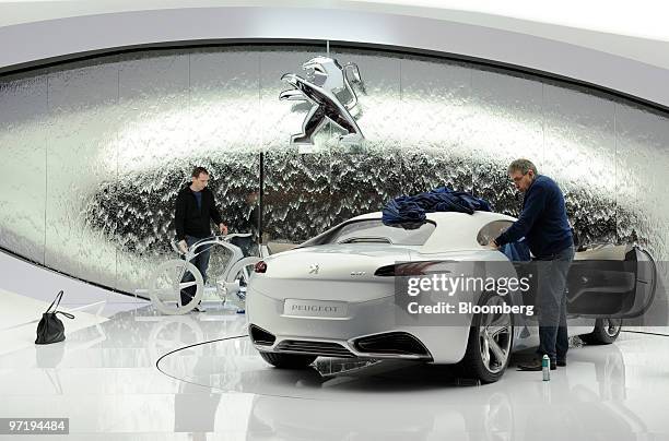 An employee cleans a Peugeot SR1 automobile prior to the official opening of the Geneva International Motor Show in Geneva, Switzerland, on Monday,...