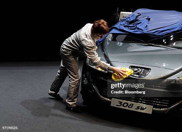 An employee cleans a Peugeot 308 SW automobile prior to the official opening of the Geneva International Motor Show in Geneva, Switzerland, on...