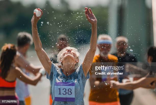 senior-marathon-läufer erfrischend selbst mit wasser während eines rennens. - marathon stock-fotos und bilder