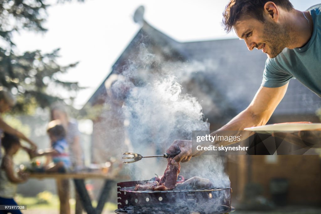 幸せな男は、屋外バーベキュー グリルで肉を焼きます。