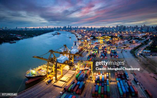 aerial view of international port with crane loading containers in import export business logistics with cityscape of bangkok city thailand at night - shipyard stock-fotos und bilder