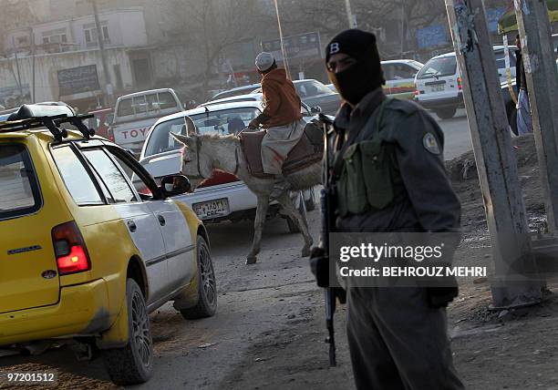 An Afghan boy rides his donkey as a policeman stands guard at a check point in a neighborhood of the capital Kabul on March 1, 2010. Taliban car...