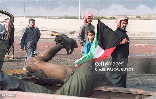 Kuwaiti holding Kuwaiti flag, looks 27 February 1991 in Kuwait City at the body of Iraqi killed during fighting between allied forces and Iraqi army...