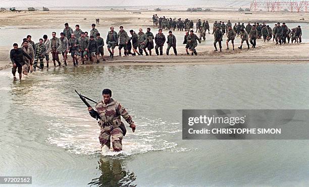 Saudi Arabian soldier leads Iraqi prisoners through a pool of water in the Kuwaiti desert 25 February 1991 as allied forces continue to advance on...