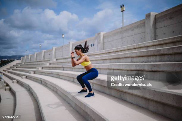 woman listening to music and exercising on urban stairs - squat stock pictures, royalty-free photos & images