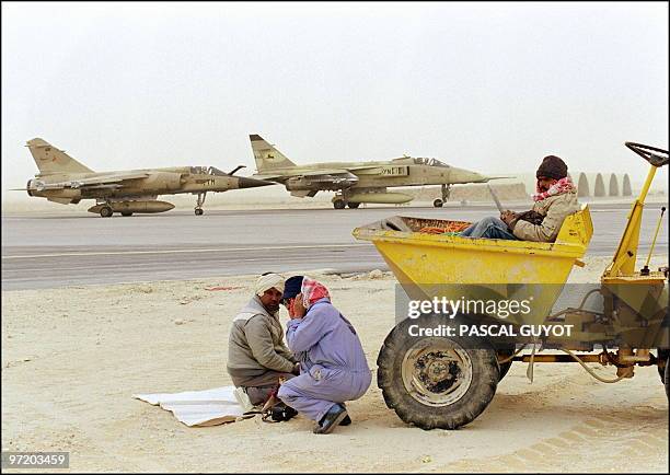 Saudi Arabian airfield workers protect their ears from noise while two French Air Force jet fighters, a French-made Mirage 2000 and...