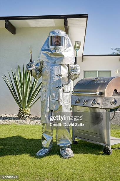 man in fire-protective suit standing next to grill - protection humour stock-fotos und bilder