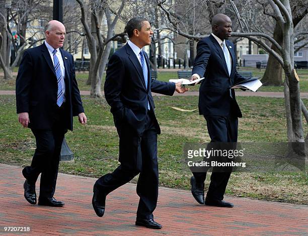 President Barack Obama, center, receives a paper from aide Reggie Love, right, as they walk through Lafayette Park on their way back to the White...