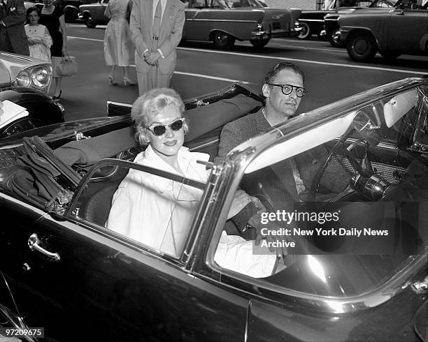 Actress Marilyn Monroe clings to arm of husband Arthur Miller as they prepared to zoom away in his sports car from 444 E. 57th St., for short...