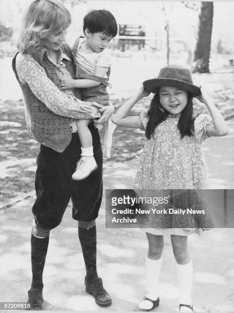 Actress Mia Farrow holds son Misha in her arms as daughter Soon Yi Previn tries on mom's hat in Central Park.