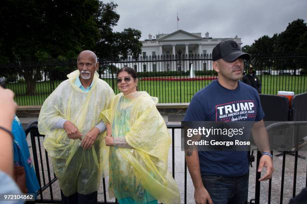 Crowd of people wearing plastic ponchos and carrying umbrellas and a man in a Trump t-shirt stroll around the mall in front of The White House on...