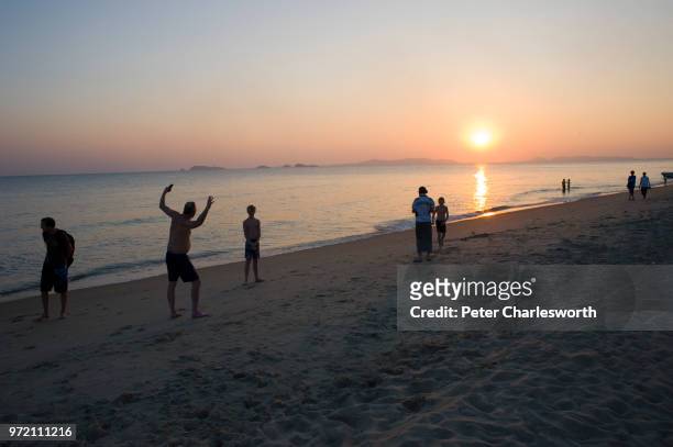 Tourists play on the beach at sunset.