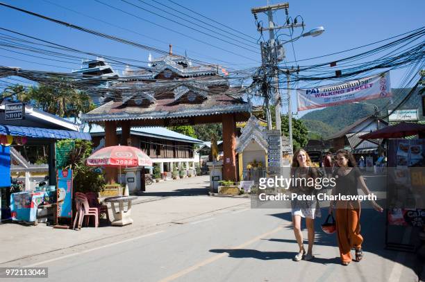 Tourists walk down a small street blighted by electricity and telephone poles and wires in the ever growing town of Pai, once a small village in the...