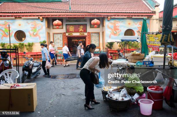 Vendor sells food from her baskets at her small street-side pitch opposite a Chinese temple in the Chinatown district of Chiang Mai.