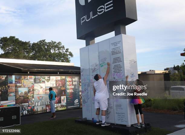 Jim McDermott and Isabella Andriolo write messages on the Pulse sign as they visit the memorial to the 49 shooting victims setup at the Pulse...