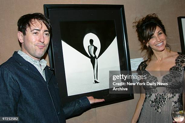 Alan Cumming and Gina Gershon admire "Versace Dress," a photograph by Herb Ritts, during a benefit at Sotheby's to posthumously recognize the...