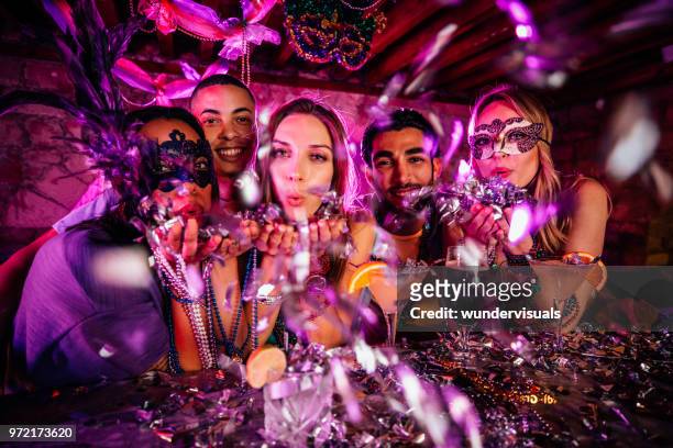 happy friends celebrating mardi gras and blowing confetti at party - fiesta stock pictures, royalty-free photos & images