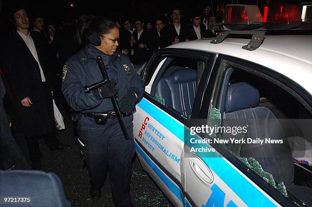 Cop surveys damage to a police cruiser along 16th Ave. In the Borough Park section of Brooklyn during protests after claims police roughed up an...