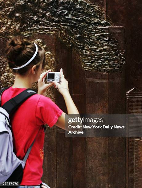 Young woman takes a photograph of the first permanent Ground Zero memorial to the FDNY's lost heroes of 9/11, a 56-foot-long bronze bas-relief...