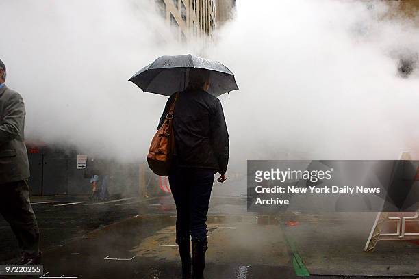 Woman wards off the rain with an umbrella as she walks through steam pouring out of a vent at Greenwich and Rector Sts., in lower Manhattan.