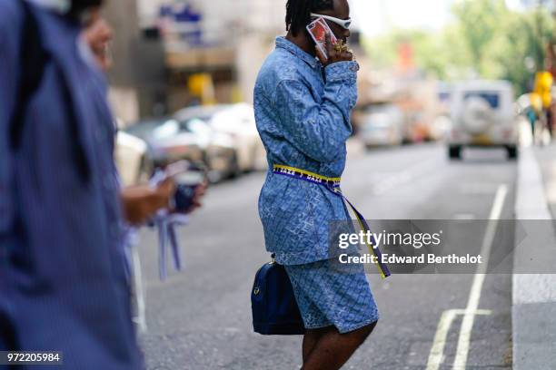 Guest wears a blue jacket, a blue and yellow striped belt, blue shorts, sunglasses, during London Fashion Week Men's June 2018 on June 09, 2018 in...