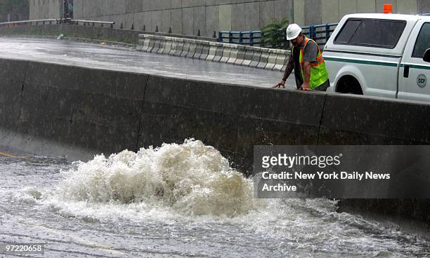 Department of Environmental Protection worker looks over the median on the Brooklyn-Queens Expressway as water gushes out of a storm drain near...