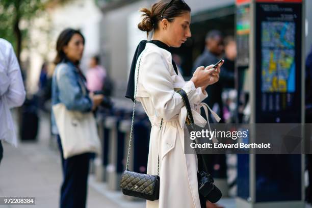 Guest wears a white jacket, a black Chanel bag, holds a Nikon camera, a mobile phone, during London Fashion Week Men's June 2018 on June 09, 2018 in...