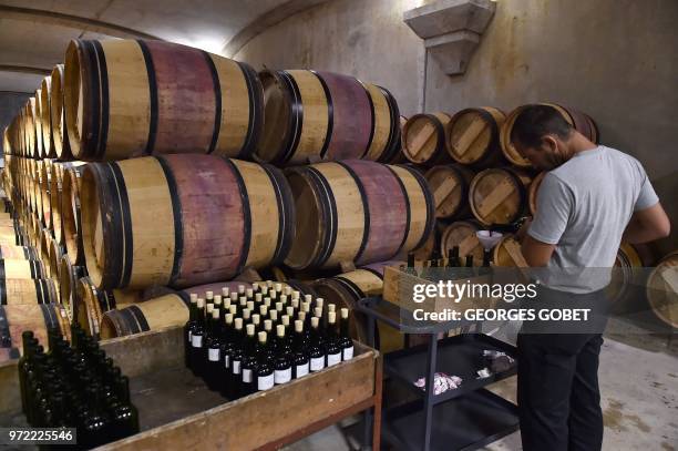 An employee pours wine into bottles as he prepares samples in the wine cellar of Chateau Margaux on June 11, 2018 in Margaux, near Bordeaux, western...