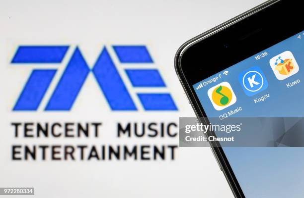 In this photo illustration the logos of QQ Music, Kugou and Kuwo are seen on the screen of an iPhone in front of a computer screen showing a Tencent...
