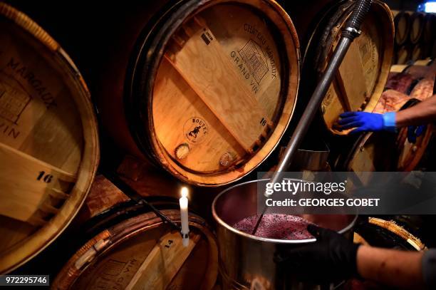 An employee uses the light of a candle to check the colour of wine in the wine cellar of Chateau Margaux on June 11, 2018 in Margaux, near Bordeaux,...