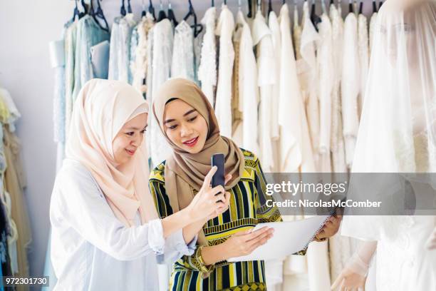 muslim women in wedding dress store using mobile phone and catalog - wedding vendor stock pictures, royalty-free photos & images