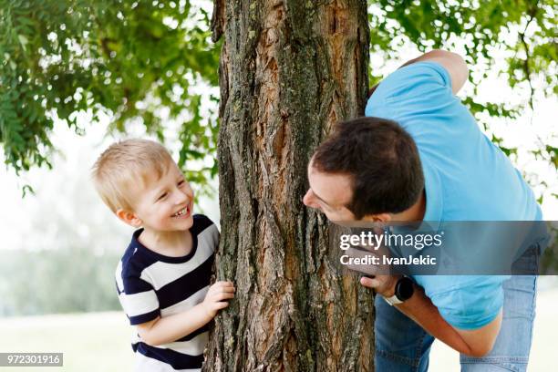 father and son playing behind the tree - ivan jekic stock pictures, royalty-free photos & images