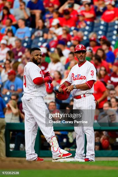 Carlos Santana of the Philadelphia Phillies takes off his gloves next to first base coach Jose David Flores at the end of the first inning against...