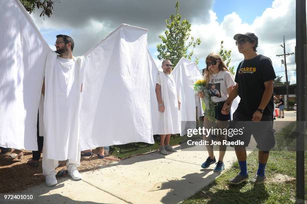 Jillienne Riethmiller and Zachary Guadalupe walk past people dressed as angels standing in front of the memorial set up for the shooting victims at...