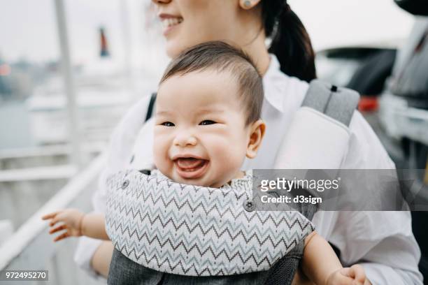 close up of smiling mother and happy baby having a good time outdoors in city - baby carrier stock pictures, royalty-free photos & images