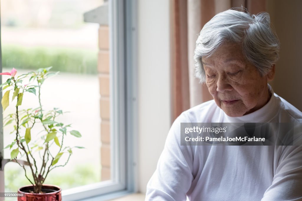 Lonely, Senior Woman Sitting by Window with Eyes Closed