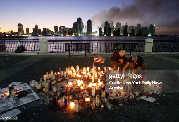 As the sun rises over smoldering ruins of World Trade Center, Jose Cruz and Alfredo Jimenez light a candle at a memorial in Jersey City, N.J....