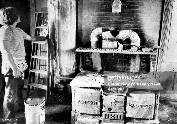 Edith Bouvier Beale house in East Hampton, L.I. Young worker seems impressed by antique stove and hot water tank in the main kitchen.