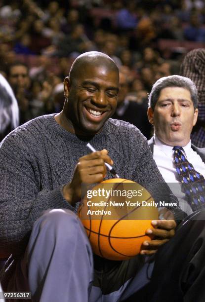 Basketball legend Earvin Johnson autographs ball for a fan while attending a game between the New Jersey Nets and the Portland Trail Blazers at the...